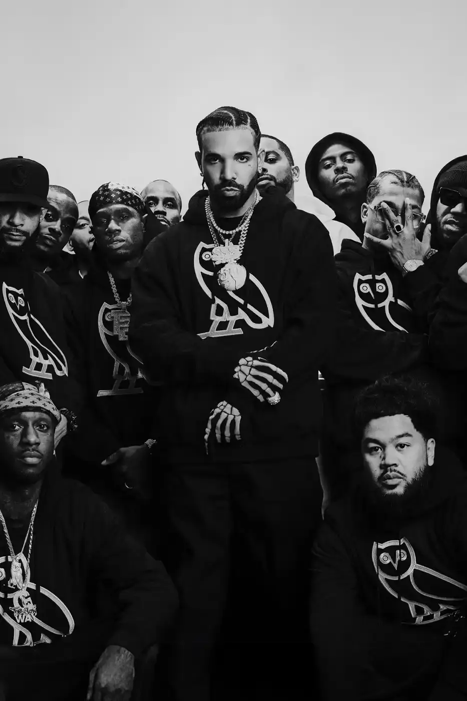 Drake and his OVO team members pose together wearing black hoodies with the OVO owl logo for the new "OG" campaign. The image shows Drake in the center, surrounded by his close associates including Jonny Roxx and Niko Carino. They stand against a plain background, emphasizing the group's unity and the branded clothing. Additional images feature individual shots of each team member modeling various pieces from the new OVO collection, including a letterman jacket and other sweater designs