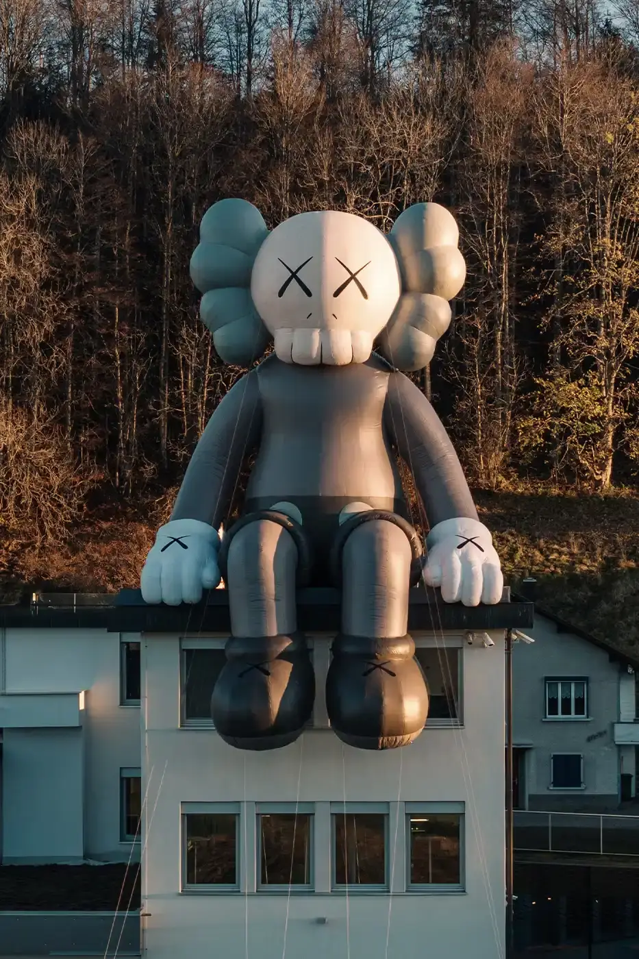 AllRightsReserved A massive 11-meter tall KAWS COMPANION sculpture in grey-toned color sits on the rooftop of the Audemars Piguet headquarters. The sculpture overlooks the glass spiral museum building in Le Brassus, Switzerland, against a mountainous backdrop, symbolizing the intersection of art and traditional watchmaking craftsmanship. (image 9 of 9)