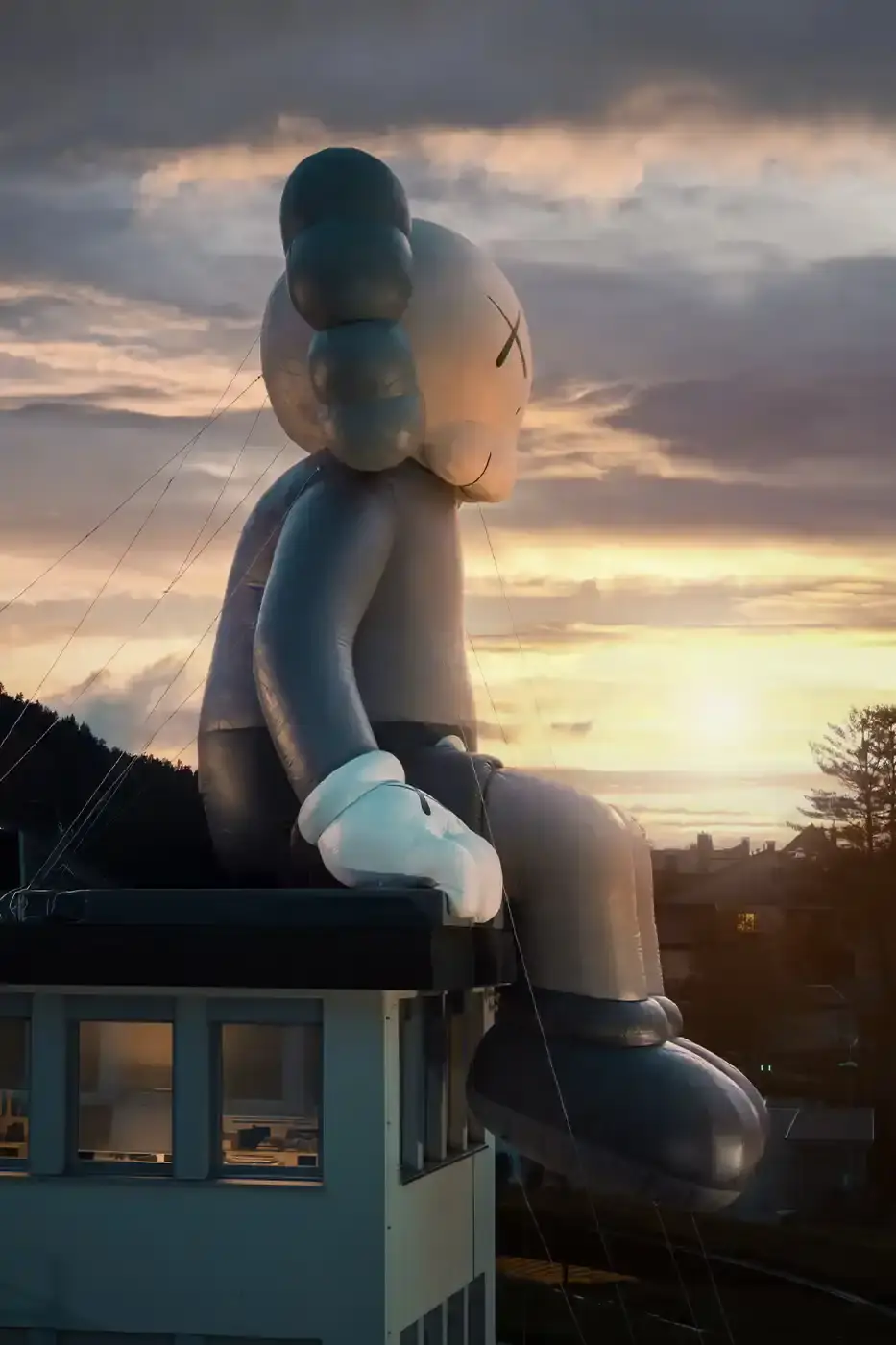 AllRightsReserved A massive 11-meter tall KAWS COMPANION sculpture in grey-toned color sits on the rooftop of the Audemars Piguet headquarters. The sculpture overlooks the glass spiral museum building in Le Brassus, Switzerland, against a mountainous backdrop, symbolizing the intersection of art and traditional watchmaking craftsmanship. (image 2 of 9)