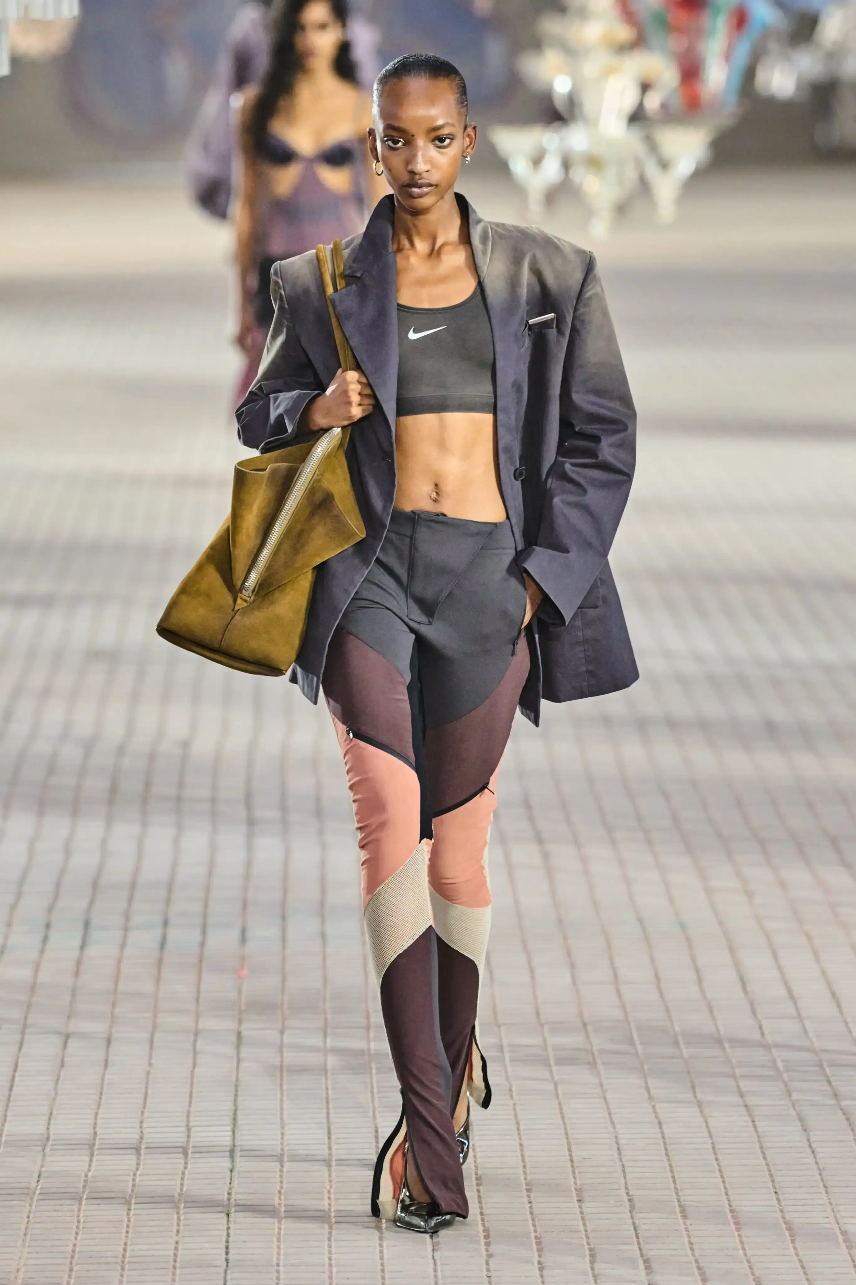The Attico's Spring/Summer 2025 runway show at Milan Fashion Week features a surprising collaboration with Nike. Models walk on an industrial set adorned with colorful glass chandeliers, showcasing a collection that blends high fashion with sportswear elements. The runway presentation, titled "The Sound of Breaking Glass," explores themes of fragility and strength through contrasting designs. Sheer fabrics, form-fitting silhouettes, and embroideries are juxtaposed with nylon materials, bomber jackets, and cargo pants. The color palette is predominantly dusty and faded. Select Nike athletic wear pieces are integrated into the collection, symbolizing resilience and personal growth. Designers Gilda Ambrosio and Giorgia Tordini aim to empower women with this innovative fusion of luxury fashion and athletic functionality, challenging traditional runway norms