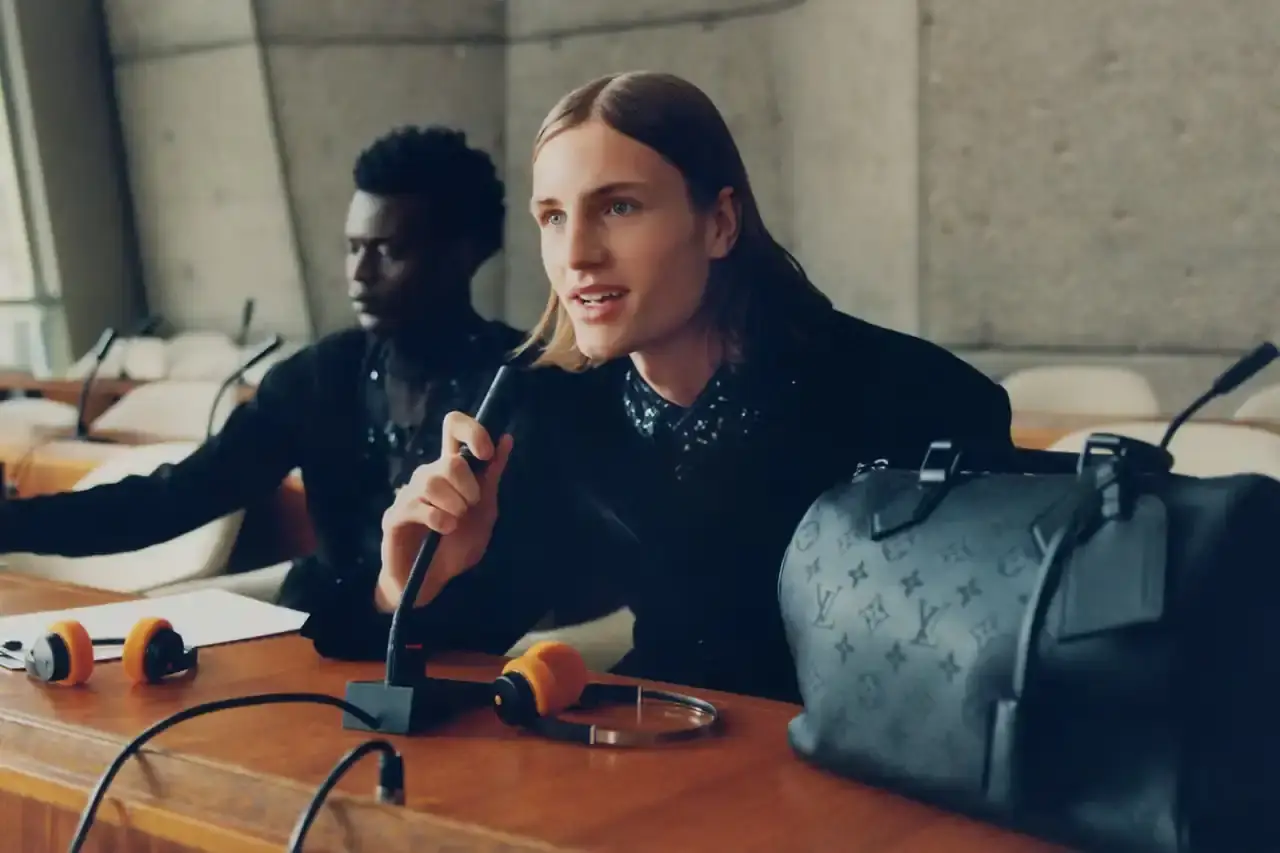 Stef Mitchell Models wearing Louis Vuitton Spring 2025 collection pose in UNESCO's headquarters. They're dressed in earth-toned suits and casual wear, photographed in formal meeting rooms and gardens. The images showcase bags, sunglasses, and diplomatic-inspired fashion against modernist architecture. (image 14 of 15)