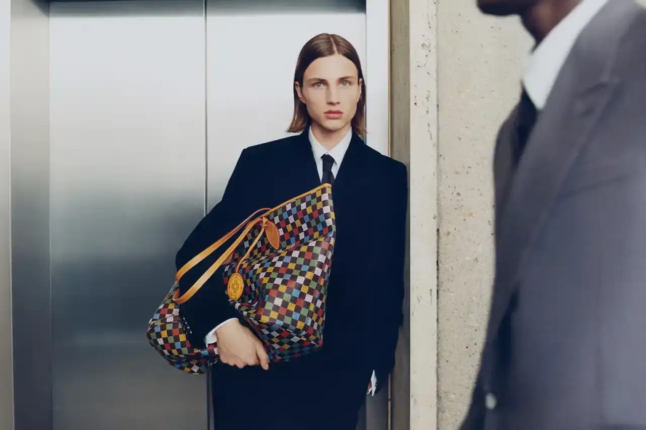 Stef Mitchell Models wearing Louis Vuitton Spring 2025 collection pose in UNESCO's headquarters. They're dressed in earth-toned suits and casual wear, photographed in formal meeting rooms and gardens. The images showcase bags, sunglasses, and diplomatic-inspired fashion against modernist architecture. (image 10 of 15)